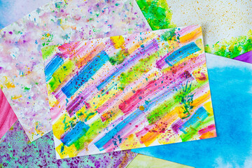 Top view of pile sheets paper with handmade colorful watercolor drawings