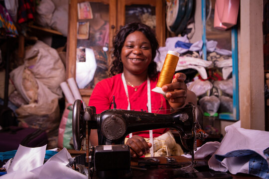 an African seamstress holds a bobbin in her hand and works in her tailor shop, she is happy and smiling