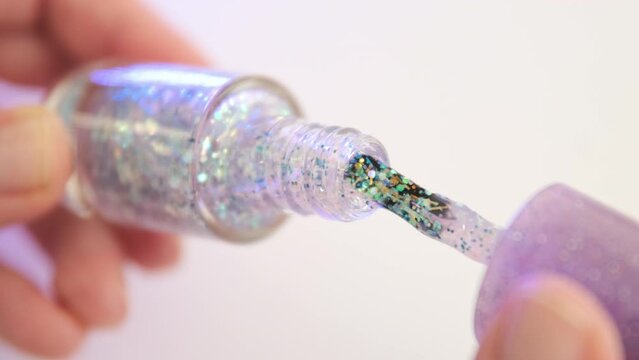 Taking out brush from glitter nail polish bottle. Shine shellac gel polish for design manicure decor nail.