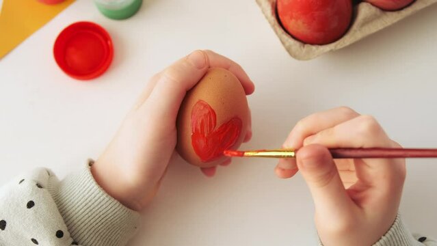 Little child decorates Easter eggs with colored food paint. Hand craft preparing for the feast of the holy Easter. Flat lay, top view.	