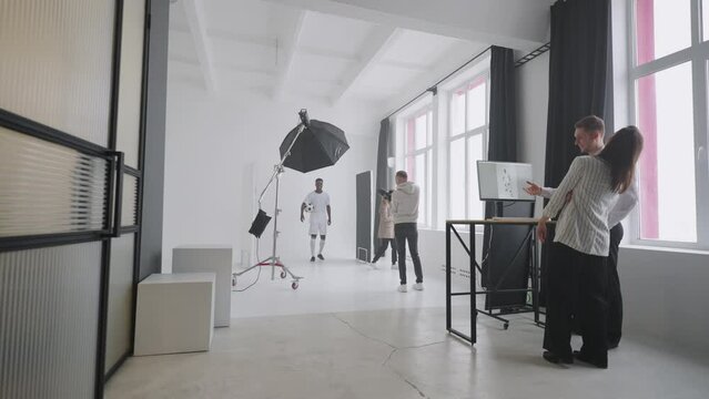 editors are discussing pictures on sportive photosession for magazine, black footballer is posing