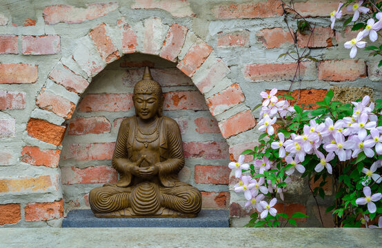 Terracotta Buddha statue in front of a rough brick wall with a Clematis montana on the side