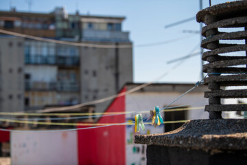Close-up on colorful laundry pins (clothes pegs) hanging on rope, on flat rooftop. Drying laundry on hot summer day.