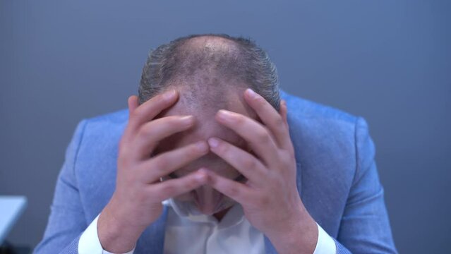 Bald man wearing a wig.
The man with the wigs in front of him puts one on his head, doesn't like it and gets angry and throws it away.
