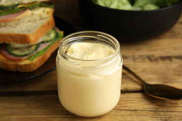 Jar of delicious mayonnaise near fresh sandwiches on wooden table