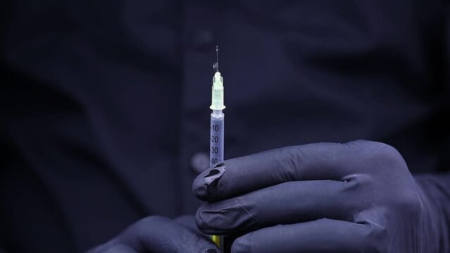 hands holding an ampoule and a syringe for injection