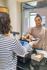 Happy african american woman making payment with credit card on payment terminal in sustainable local shop standing before counter.