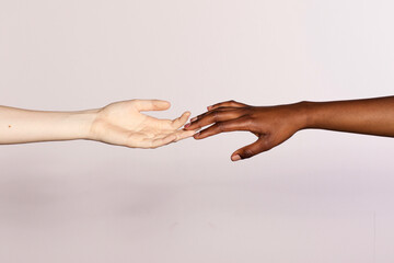Black hand and a white hand reaching for each other on a white background- racial equality concept - obrazy, fototapety, plakaty