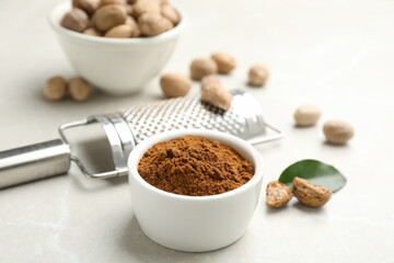 Nutmeg powder and seeds near grater on white table