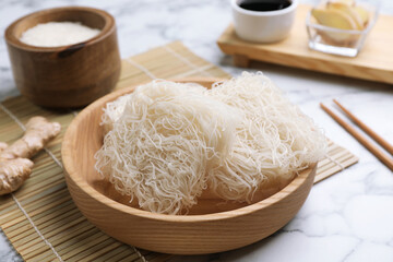 Bowl with uncooked rice noodles on white marble table