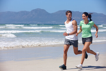Getting fit together. Shot of a young couple jogging together on the beach.
