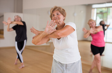 Portrait of an elderly dancing woman practicing vigorous swing at a group training session in the studio of dance