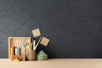 Table at home office with supplies and black wall copy space. Stylish workspace.	