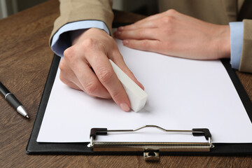 Woman erasing something on paper at wooden table, closeup