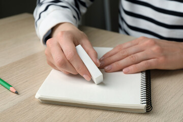 Woman erasing something in notebook at wooden table, closeup