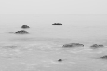 Tranquil scenery of rocks in the sea on a foggy day, grayscale shot