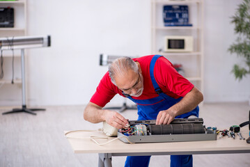 Old repairman repairing air-conditioner at workshop