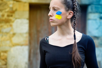 russian war against ukraine. young girl with braid and face painted in the colors of the ukrainian...