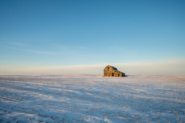 Old barn in a winter field in Alberta, Canada with blue sky.