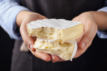 Woman with pieces of delicious brie cheese on black background, closeup