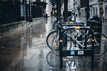 Closeup of bicycles parked in racks on the pavement on a rainy day in London, England