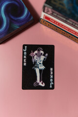 Top view shot of a black joker playing card on a pink background with other board games - obrazy, fototapety, plakaty