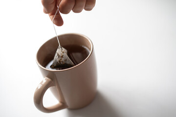 person's hand holding a tea bag and making hot cup of tea