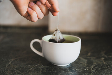 person's hand holding a tea bag and making hot cup of tea