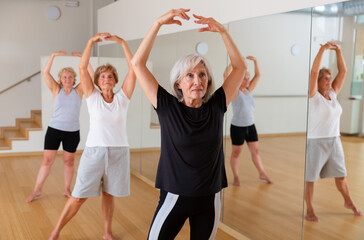 Aged women performing ballet dance during their group training in fitness room.