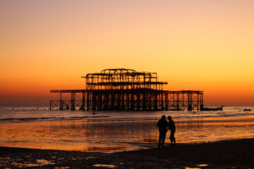 Low tide sunset view of Brighton's derelict west pier with silhouettes. Brighton, United Kingdom.