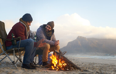 Its warming up fast. Two young men sitting around a fire on the beach.
