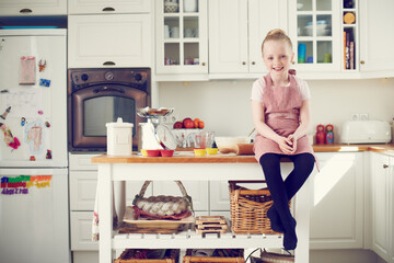 Ready to learn some baking skills. Cute little girl sitting on the kitchen counter ready to start baking.