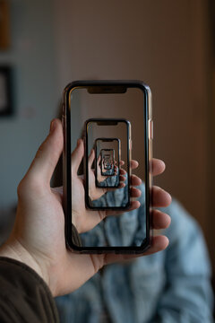 A Person Holding A Phone With Many Trippy Mirroring Repetitions Of The Same Image On The Screen.