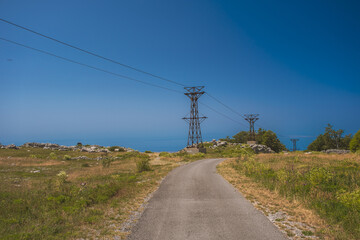 Empty road leading to an island in Croatia surrounded by electrical pylons on a sunny day