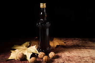 A bottle of walnut wine inserted on a wooden table that has walnuts and leaves on it