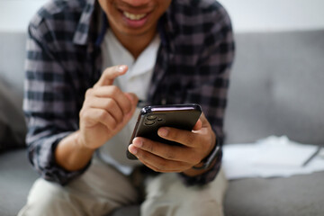 Cropped shot happy asian man sitting on couch and using smart phone.