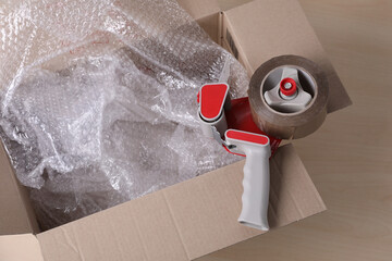 Cardboard box with bubble wrap and adhesive tape on wooden table