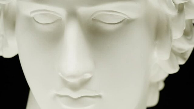 Plaster head sculpture Apollonian close-up. Gypsum ancient statue isolated on black background.