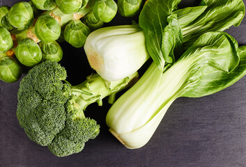 Top view of ripe broccoli, brussels sprout and bok choy on a dark wooden table