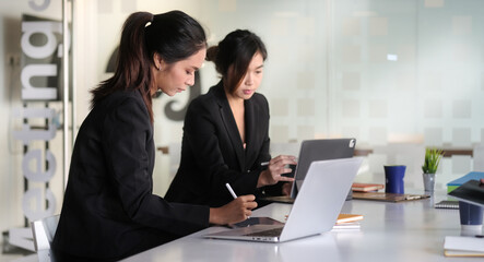Fototapeta premium Two female business colleagues sitting in boardroom and discussing business strategy together.