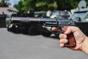 A combat pistol with a silencer in a man's hand. Against the background of military armored...