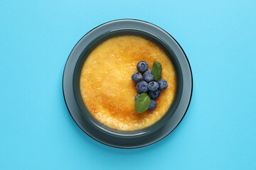 Delicious creme brulee with fresh blueberries and mint on light blue background, top view