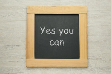 Small chalkboard with motivational quote Yes you can on white wooden background, top view