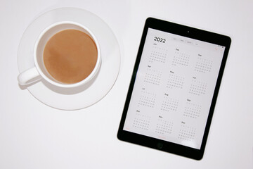Top view of a cup of coffee and a tab displaying calendar