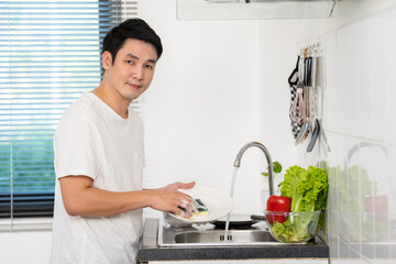 happy man washing dishes in the sink in the kitchen at home