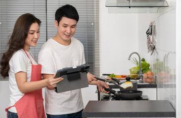 couple cooking and preparing food according to a recipe on a tablet computer in the kitchen at home