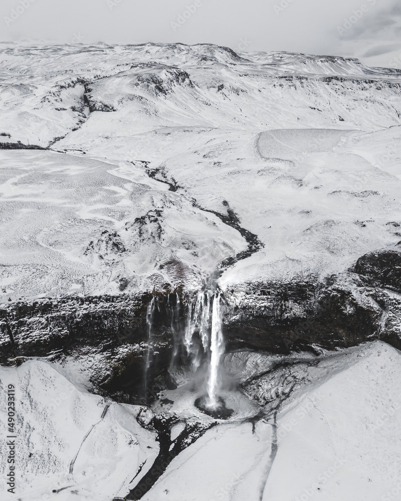 Poster vertical shot of a mesmerizing snowy landscape with a waterfall in iceland