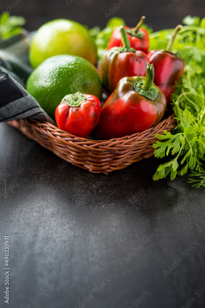 Poster Selective focus shot of an assortment of fresh red peppers, limes, and coriander in a basket