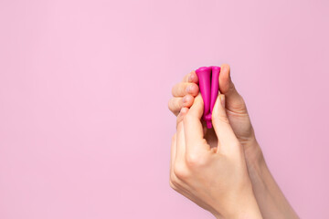 Mature content A young woman folding a pink menstrual cup in her hand. Pink colored background. Space for text. Eco-friendly silicone women's health cycle