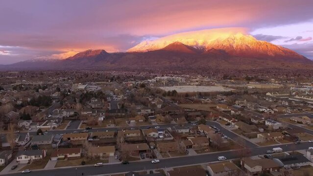 Flying over houses in Orem city with Timpanogos Mountain glowing during sunset in Utah.